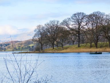 A lake with a person in a rowboat near a shoreline with leafless trees at Buttermere Sawrey near Hawkeshead