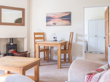 A dining area with two wooden chairs and a table near a fireplace with a wicker basket and a mirror above at Buttermere Sawrey near Hawkeshead