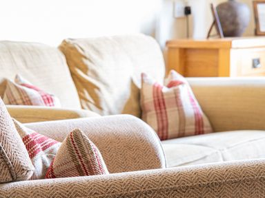 A close up of beige couches with red and beige patterned cushions and a wooden cabinet in the background at Buttermere Sawrey near Hawkeshead
