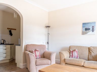 A living room with armchair and sofa with plaid cushions near an archway to a kitchen at Buttermere Sawrey near Hawkeshead