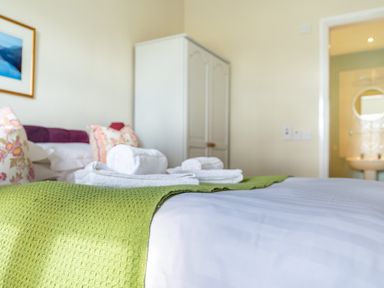 A bedroom with a bed with a green throw and folded towels near a white wardrobe and bathroom at Buttermere Sawrey near Hawkeshead