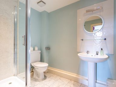 A bathroom with a shower, toilet, sink, round mirror, and soap dispenser at Buttermere Sawrey near Hawkeshead
