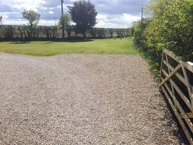 A gravel driveway with a wooden gate and green lawn with trees and bushes at Wold Cottage in Hunmanby