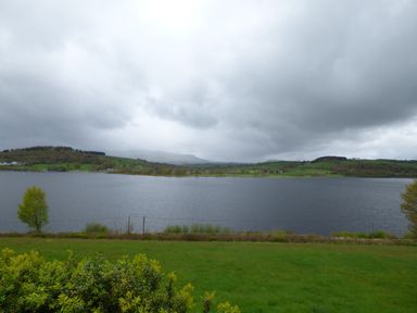A body of water with green hills and cloudy sky at Ffynnon Gower in Llangower near Bala