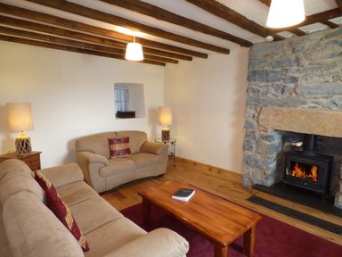 A living room with beige sofas a wooden coffee table and a stone fireplace at Ffynnon Gower in Llangower near Bala