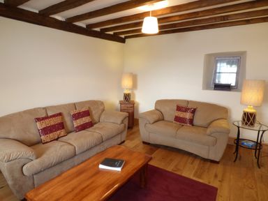 A living room with two beige sofas a wooden coffee table wooden beams on the ceiling and two lamps at Ffynnon Gower in Llangower near Bala