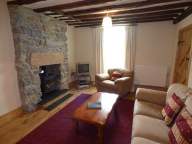 A living room with stone fireplace wooden ceiling beams and beige armchairs at Ffynnon Gower in Llangower near Bala