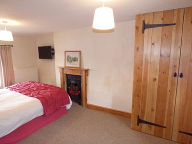 A bedroom with a bed a fireplace a wall-mounted TV and wooden closet doors at Ffynnon Gower in Llangower near Bala