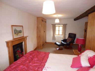 A bedroom with a bed covered in pink bedding a black reclining chair with footstool a small window with curtains and wooden wardrobes at Ffynnon Gower in Llangower near Bala