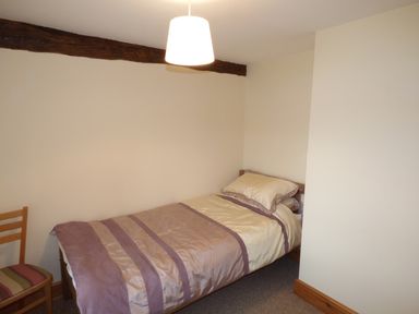 A small bedroom with a single bed and a wooden chair at Ffynnon Gower in Llangower near Bala