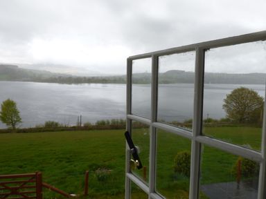 A view of a lake and grassy land through a partially open window at Ffynnon Gower in Llangower near Bala