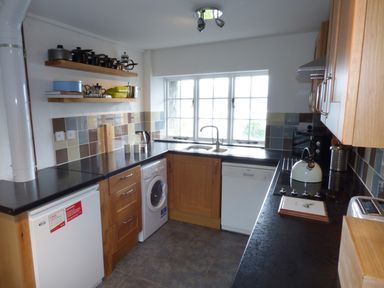 A kitchen with wooden cabinets black countertops tiled backsplash and appliances at Ffynnon Gower in Llangower near Bala
