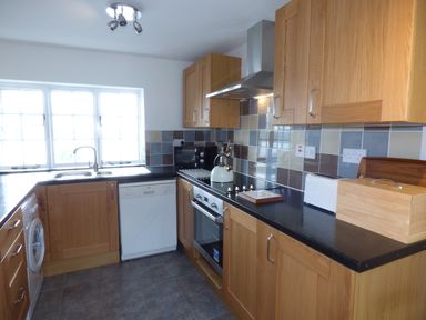 A kitchen with wooden cabinets a black countertop a stove a kettle a toaster and a window at Ffynnon Gower in Llangower near Bala