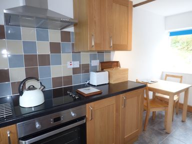 A kitchen with wooden cabinets a tiled backsplash a kettle toaster and a wooden table with chairs at Ffynnon Gower in Llangower near Bala