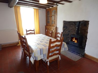 A dining room with wooden table and chairs a wood stove in a stone fireplace and a wooden cabinet at Ffynnon Gower in Llangower near Bala