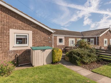 A brick residential building with windows a small garden shed and shrubs at Rock Rose Beadnell