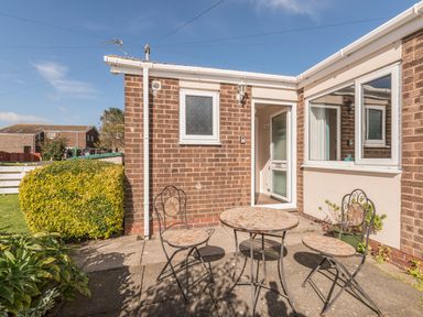 An outdoor patio with a round table and two chairs next to a brick house with an open door at Rock Rose in Beadnell