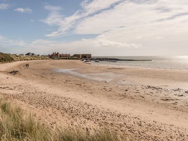 A sandy beach with small boats near a harbor and buildings in the background at Rock Rose in Beadnell