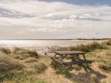 A wooden picnic table on grassy sand dunes overlooking a beach and sea at Rock Rose in Beadnell