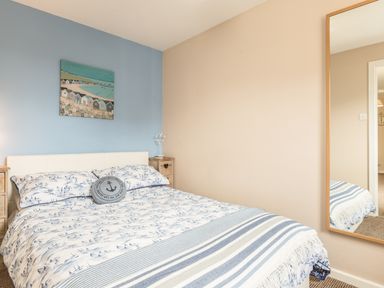 A bedroom with a bed beside two wooden nightstands and a wall mirror at Rock Rose in Beadnell