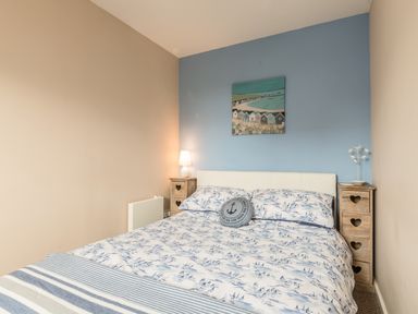 A bedroom with a bed between wooden nightstands and a painting on a blue accent wall at Rock Rose in Beadnell