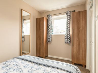 A bedroom with two wooden wardrobes a window with patterned curtains and a wall mirror at Rock Rose in Beadnell