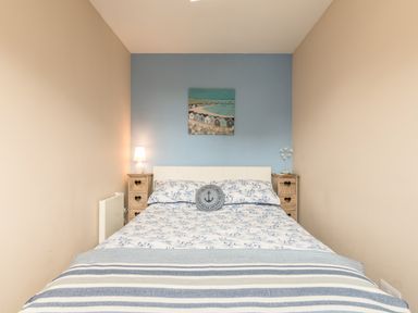 A bedroom with a blue accent wall a bed with patterned bedding and two wooden nightstands with lamps at Rock Rose in Beadnell