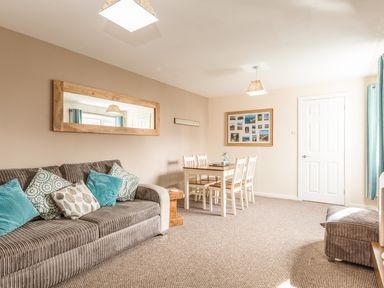 A living room with a sofa and dining table next to a white door at Rock Rose in Beadnell
