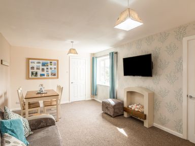 A living room with a sofa blue cushions a dining table chairs a wall mounted tv and a fireplace at Rock Rose in Beadnell