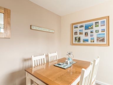 A dining area with a wooden table and four white chairs with a wall sign and photo collage at Rock Rose in Beadnell