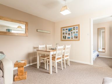 A dining area with a wooden table and six white chairs and a framed collage on the wall at Rock Rose in Beadnell