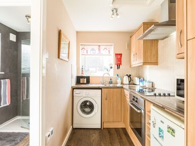 A kitchen with wooden cabinets a washing machine a stove a microwave and a view of a bathroom at Rock Rose in Beadnell