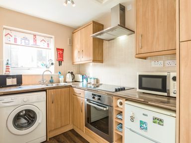 A kitchen with wooden cabinets washing machine oven microwave and refrigerator at Rock Rose in Beadnell