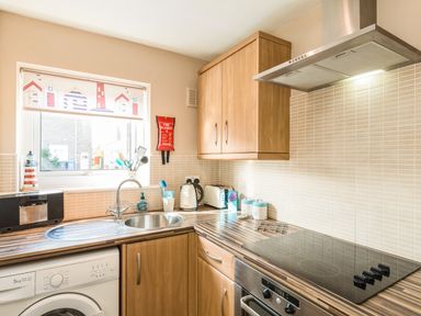 A kitchen with wooden cabinets a stainless steel sink electric stove oven and washing machine at Rock Rose in Beadnell
