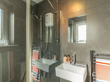 A bathroom with a shower, small sink, mirror, window, and towels at Rock Rose in Beadnell