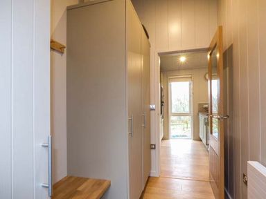 A hallway with wooden flooring and built-in storage leading to a kitchen with large window at Shepherd Lodge in Allithwaite near Grange-over-Sands