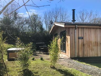 A wooden lodge with patio furniture and a hot tub in a garden at Shepherd Lodge in Allithwaite near Grange-over-Sands