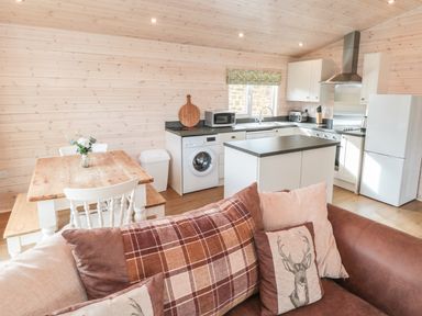 A kitchen and dining area with wooden table white chairs washing machine and brown sofa at Thorntree Lodge in Rowsley