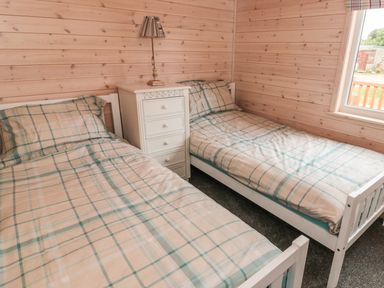A bedroom with two single beds with plaid bedding and a white nightstand with a lamp at Thorntree Lodge in Rowsley