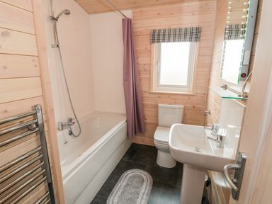A bathroom with a bathtub shower combination toilet sink mirror and window at Thorntree Lodge in Rowsley