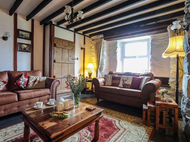 A living room with brown sofas a wooden coffee table and flowers in a vase at Hendy Cottage in Llanbedr near Harlech