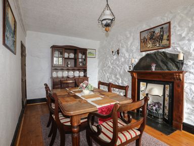 A dining room with a wooden table and chairs a cabinet with plates and a fireplace at Hendy Cottage in Llanbedr near Harlech