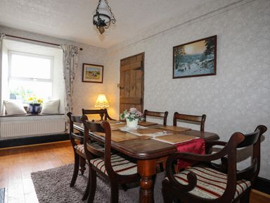 A dining room with a wooden table and chairs a window with cushions and flowers and framed pictures on the walls at Hendy Cottage in Llanbedr near Harlech