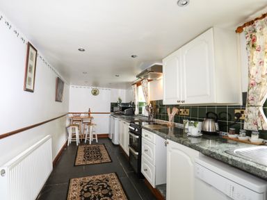 A long kitchen with white cabinets green countertops and patterned rugs at Hendy Cottage in Llanbedr near Harlech