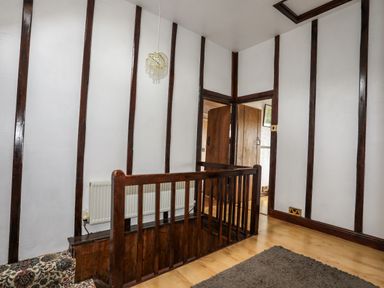 A hallway with wooden railing and patterned stairs leading downstairs at Hendy Cottage in Llanbedr near Harlech