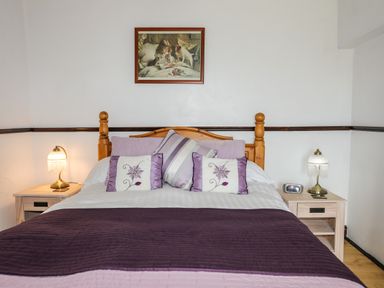 A bedroom with a wooden bed frame two bedside tables lamps and a framed picture above the bed at Hendy Cottage in Llanbedr near Harlech