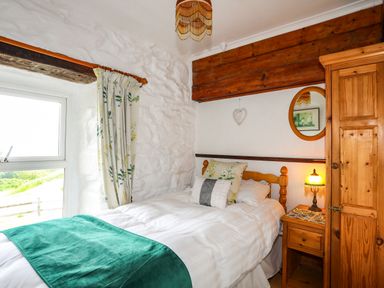 A bedroom with a wooden bed and wardrobe a window with floral curtains and a bedside table with a lamp at Hendy Cottage Llanbedr near Harlech
