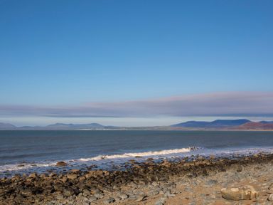 A rocky shoreline with waves and mountains in the distance at Hendy Cottage in Llanbedr near Harlech