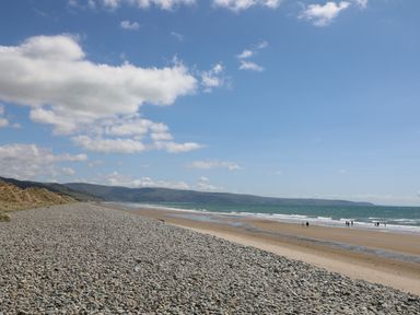 A pebble and sand beach with people near the water and hills in the background at Hendy Cottage in Llanbedr near Harlech