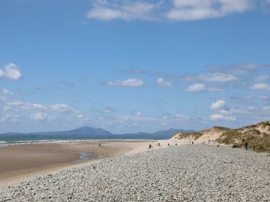 A pebble and sandy beach with dunes and people near the ocean with mountains in the background at Hendy Cottage Llanbedr near Harlech